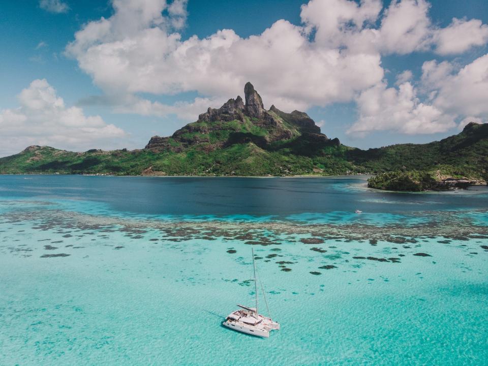 A catamaran in clear waters at Bora Bora. There's a mountain range in the back.