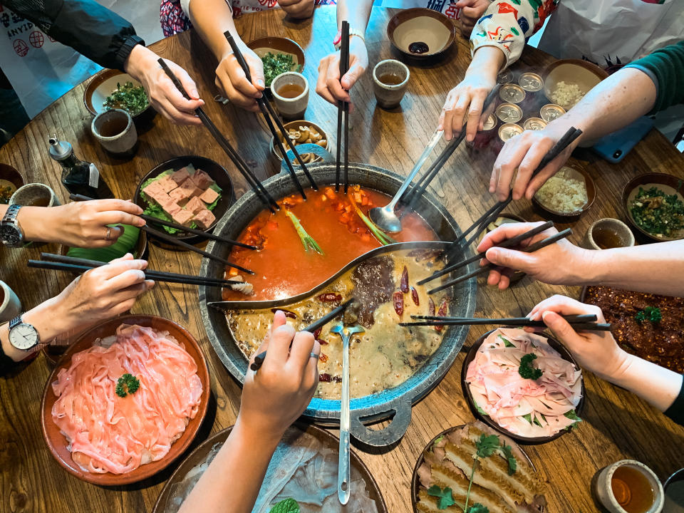 Spicy and non spicy soup, on the dining table. A variety of foodstuffs and ingredients are served beside the pot during a hotpot session.