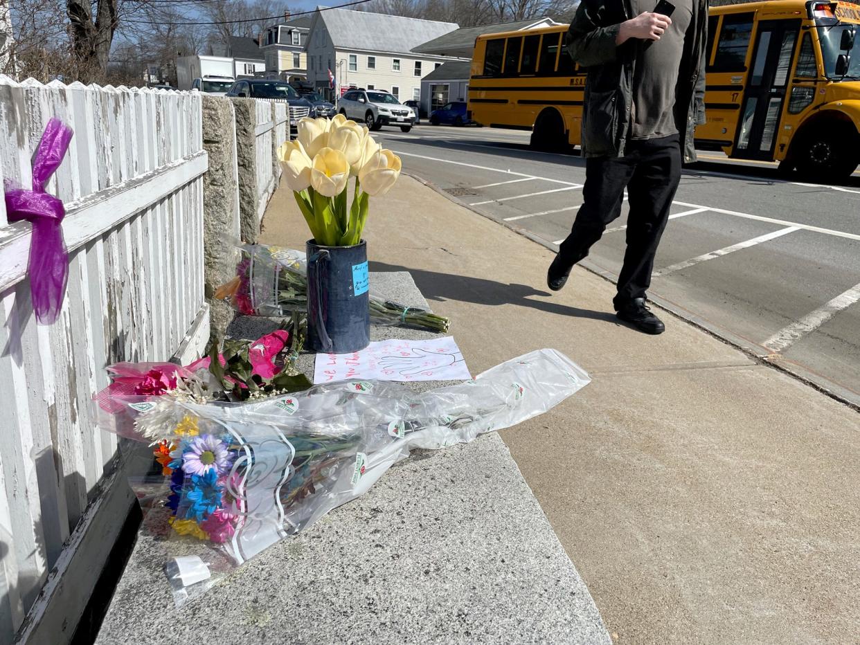 A pedestrian in South Berwick, Maine, walks by a bench Thursday, March 14, 2024, covered with flowers and notes in memory of John Nason, a local man who was seen daily watching traffic in the center of town. Nason died the previous day from a medical emergency while sitting on his favorite bench.