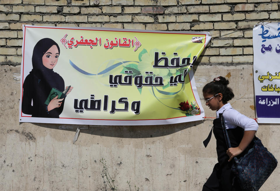 In this Thursday, March 13, 2014 photo, a schoolgirl passes by a banner for the Jaafari Personal Status Law in Baghdad, Iraq. The Arabic on the banner reads, "the Jaafari Personal Status Law saves my rights and my dignity." A contentious civil status draft law for Iraqi Shiite community that allows child marriage and restricts women’s rights has stirred up a row among many Iraqis who see it as a setback for child and women rights, threatening to add more divisions and woos to the society that is already in fragments. (AP Photo/Karim Kadim)