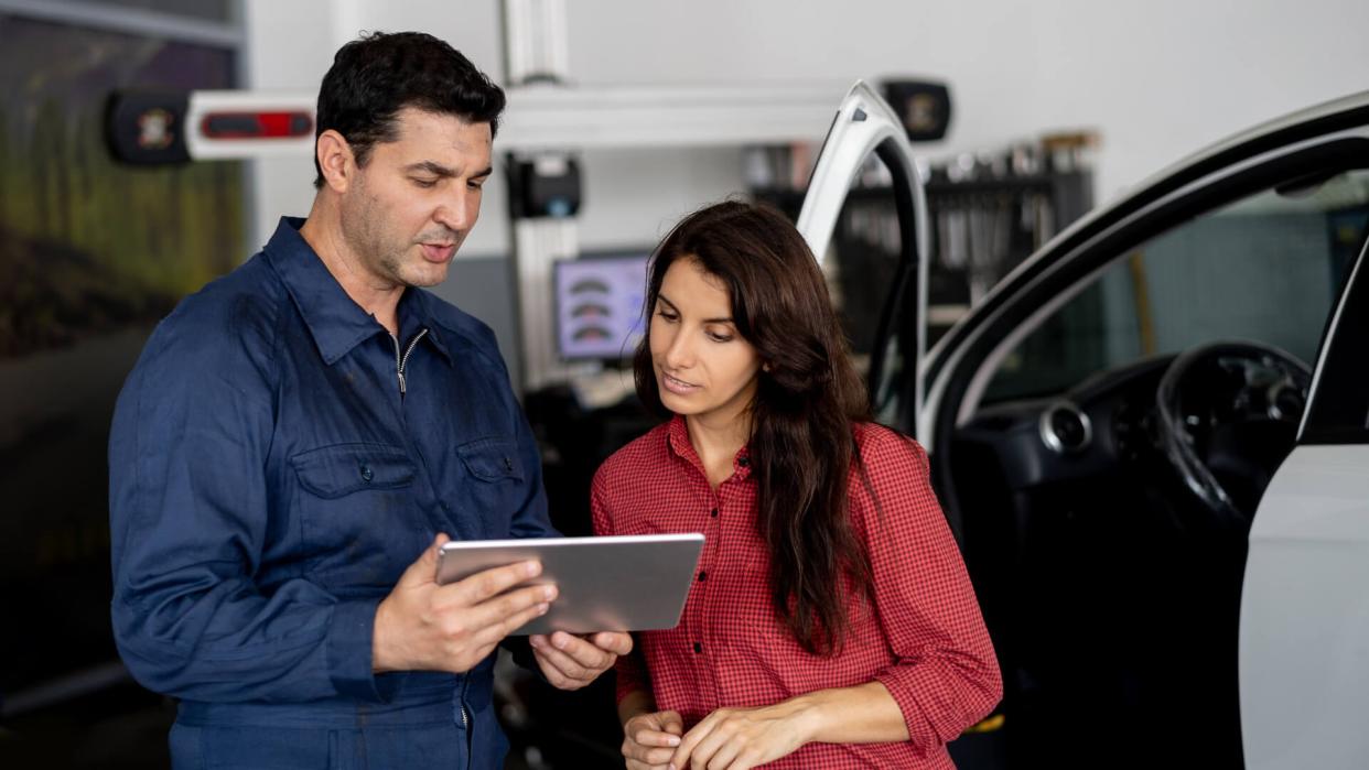 Friendly mechanic showing female customer the work done on her car on tablet at the car workshop both smiling.
