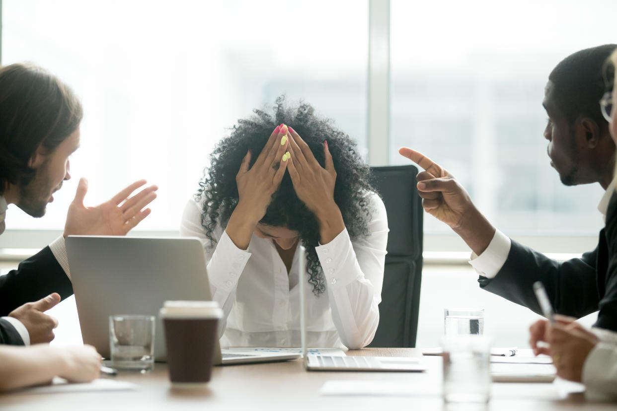 Upset depressed black woman leader suffering from gender discrimination inequality at work, diverse men colleagues pointing fingers scolding bullying frustrated african businesswoman at workplace