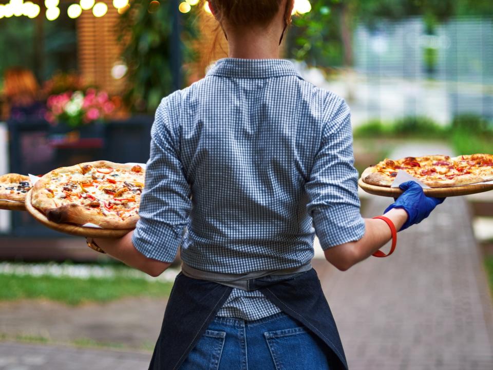 waiter with her back to us with three pizzas in her hands on the restaurant terrace