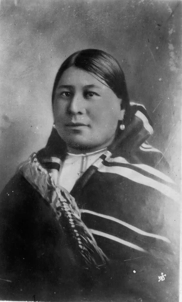 a black and white portrait of anna brown, wearing native american clothing and looking directly into the camera