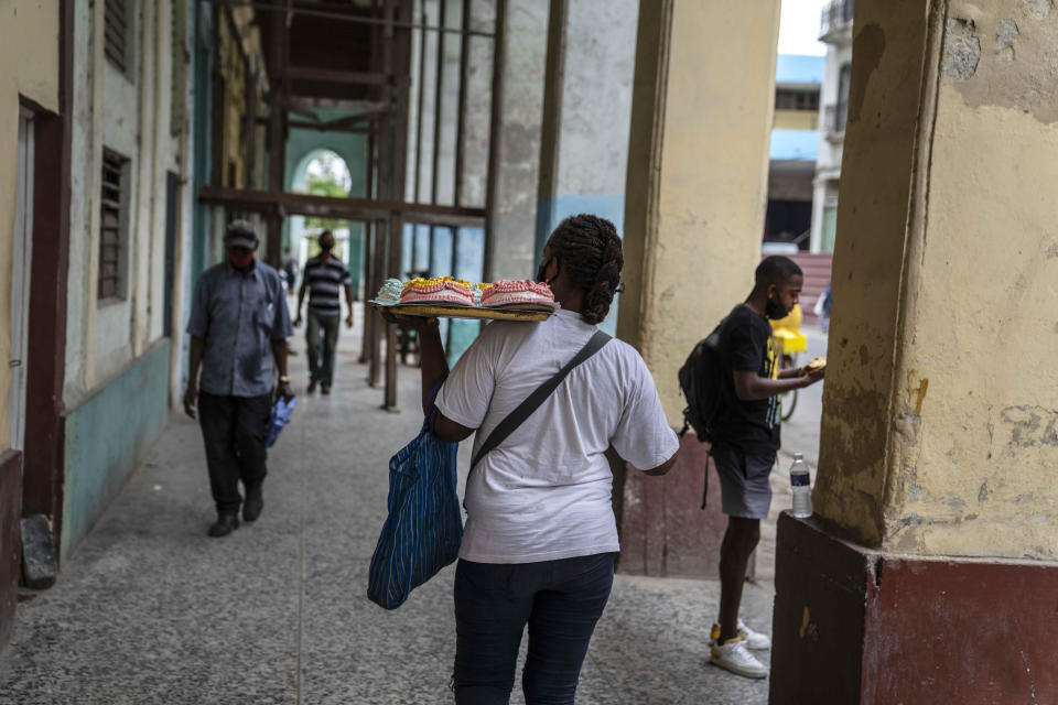 A woman walks down the street carrying a tray of cakes in Havana, Cuba, Monday, July 26, 2021 (AP Photo/Eliana Aponte)