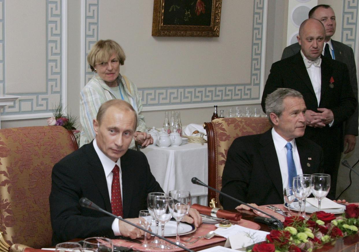 Russian President Vladimir Putin and then-U.S. President George W. Bush sit at a working dinner in 2006 as Prigozhin stands in the background. 