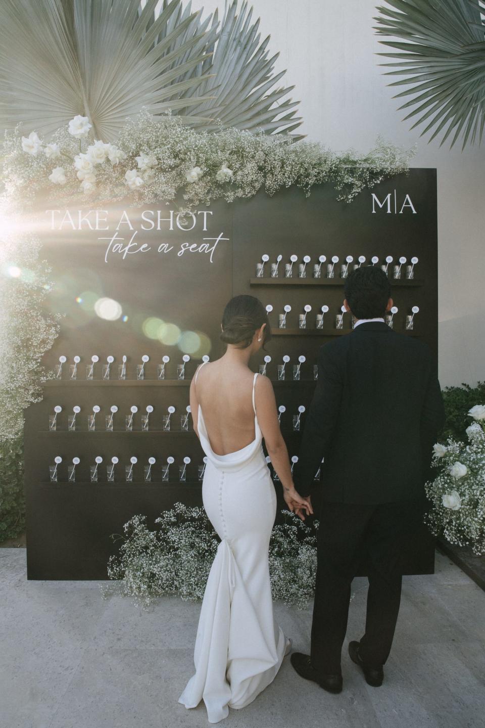 A bride and groom look at a sign that says "take a shot, take a seat."