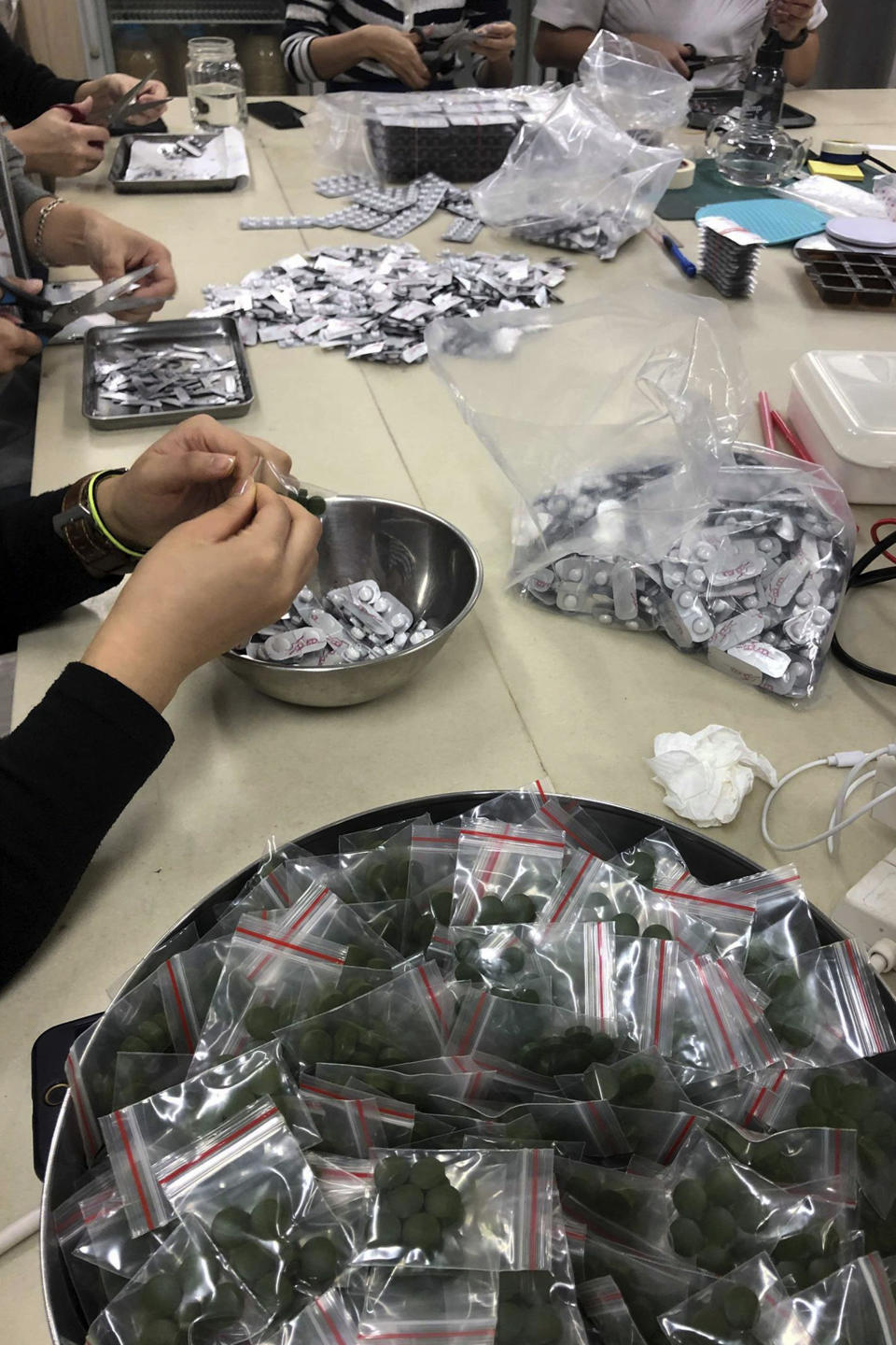 FILE - In this Sunday, Dec. 1, 2019, photo, workers pack multi-colored supplement pills in small resealable bags at an industrial building in Hong Kong. By day, the small commercial kitchen in a Hong Kong industrial building produces snacks. At night, it turns into a secret laboratory assembling a detox kit to help frontline pro-democracy protesters counter ill-effects from repeated exposure to tear gas. (AP Photo)