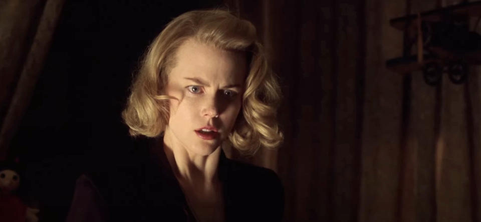 Nicole Kidman with a concerned expression, wearing a vintage-style outfit, stands against a dark background