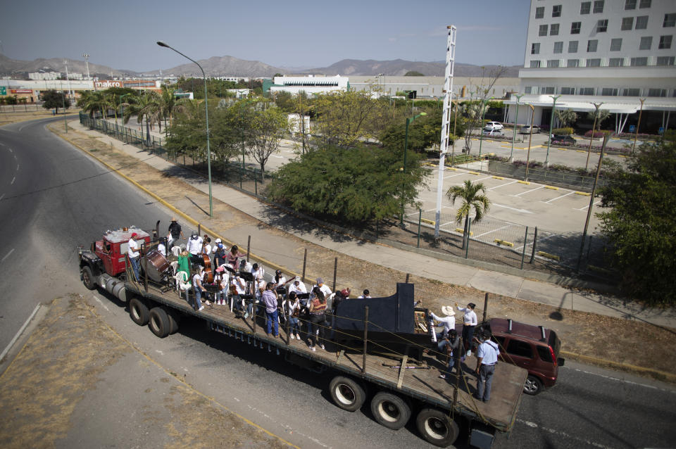 Wearing masks to curb the spread of the new coronavirus, musicians join pianist, composer and conductor Jose Agustin Sanchez on the bed of an eighteen-wheeler truck for a musical tour called "Musical Disinfection," in Barquisimeto, Venezuela, Thursday, March 4, 2021. Sanchez, who last year started playing what he calls his "Musical Vaccine" for COVID patients, is now joined by other musicians as they ride through the city playing his original compositions for anybody that wants to listen. (AP Photo/Ariana Cubillos)