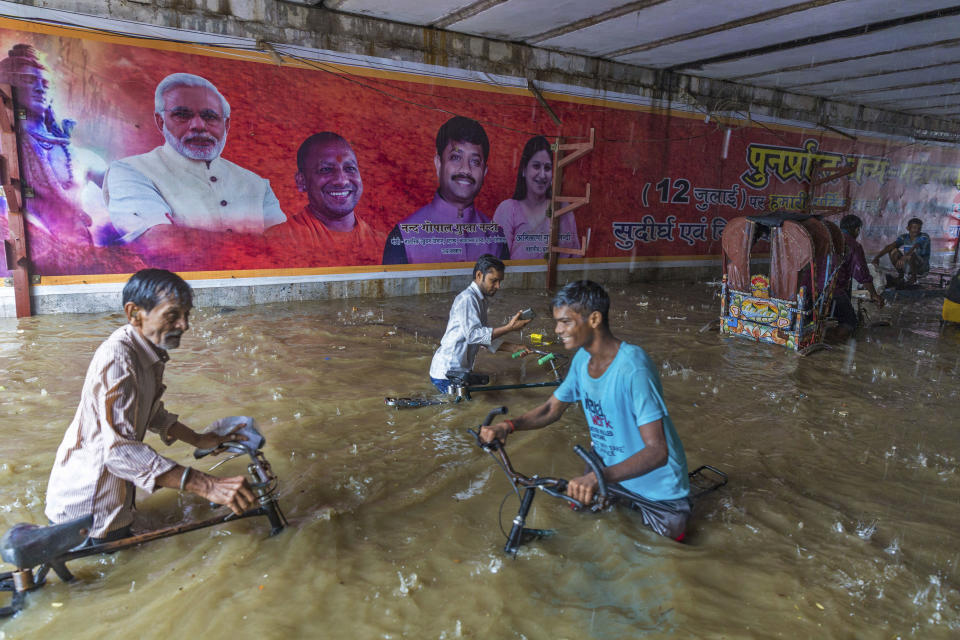 In this Sunday, Aug. 12, 2018, photo, commuters make their way through a railway under pass where posters of Indian Prime Minister Narendra Modi, left and Uttar Pradesh Chief Minister Yogi Aditya Nath are displayed following heavy rains in Allahabad, India. India gets its monsoon rains from June to September. (AP Photo/Rajesh Kumar Singh, File)