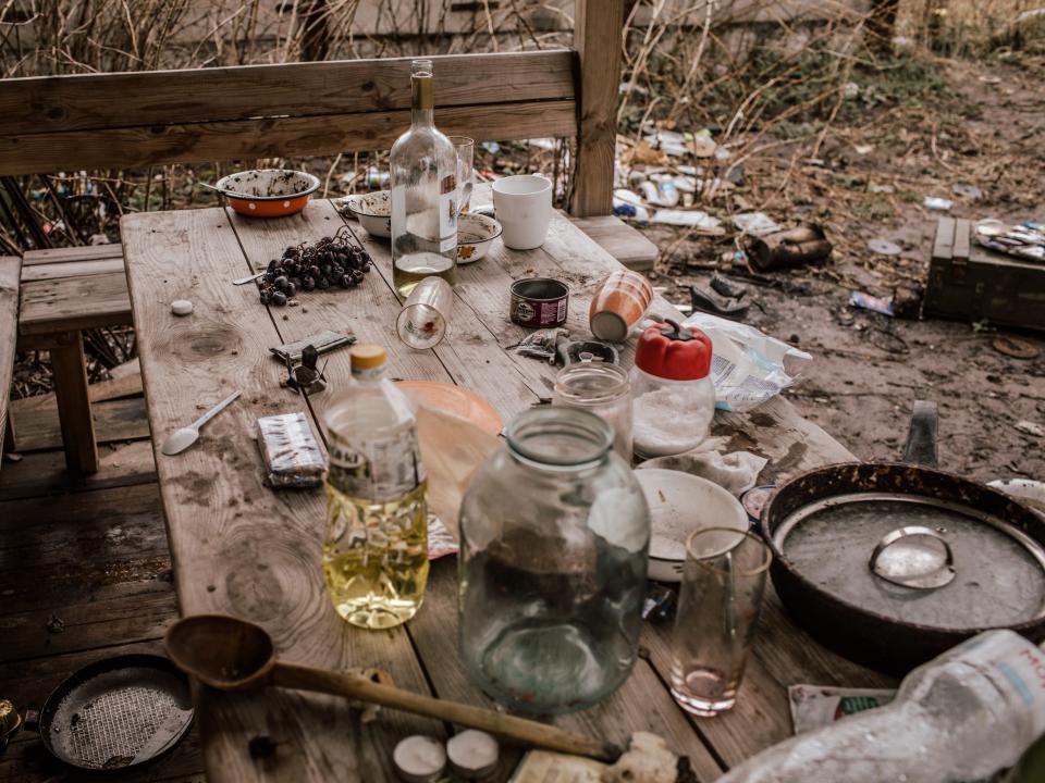 A picnic table strewn with empty glasses and empty containers.