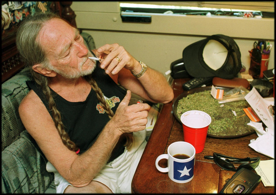 American country singer Willie Nelson takes a drag off a joint while relaxing at his home in Texas, 2000s. A large amount of marijuana is spread out on the table before him (Photo by  Liaison/Getty Images)