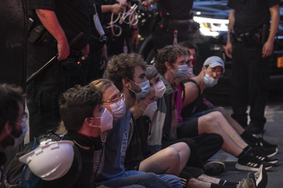 Protesters who were arrested by police for breaking a curfew during a solidarity rally calling for justice over the death of George Floyd, sit on a sidewalk as they wait to be taken away in a van on Thursday, June 4, 2020, in New York. Floyd, an African American man, died on May 25 after a white Minneapolis police officer pressed a knee into his neck for several minutes even after he stopped moving and pleading for air. (AP Photo/Wong Maye-E)