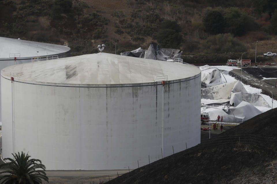 Fire and emergency crews walk past damage from a Tuesday fire at NuStar Energy fuel storage facility in Crockett, Calif., Wednesday, Oct. 16, 2019. Officials were trying to determine Wednesday if a 4.5 magnitude earthquake triggered an explosion at a fuel storage facility in the San Francisco Bay Area that started a fire and trapped thousands in their homes for hours because of potentially unhealthy air. (AP Photo/Jeff Chiu)