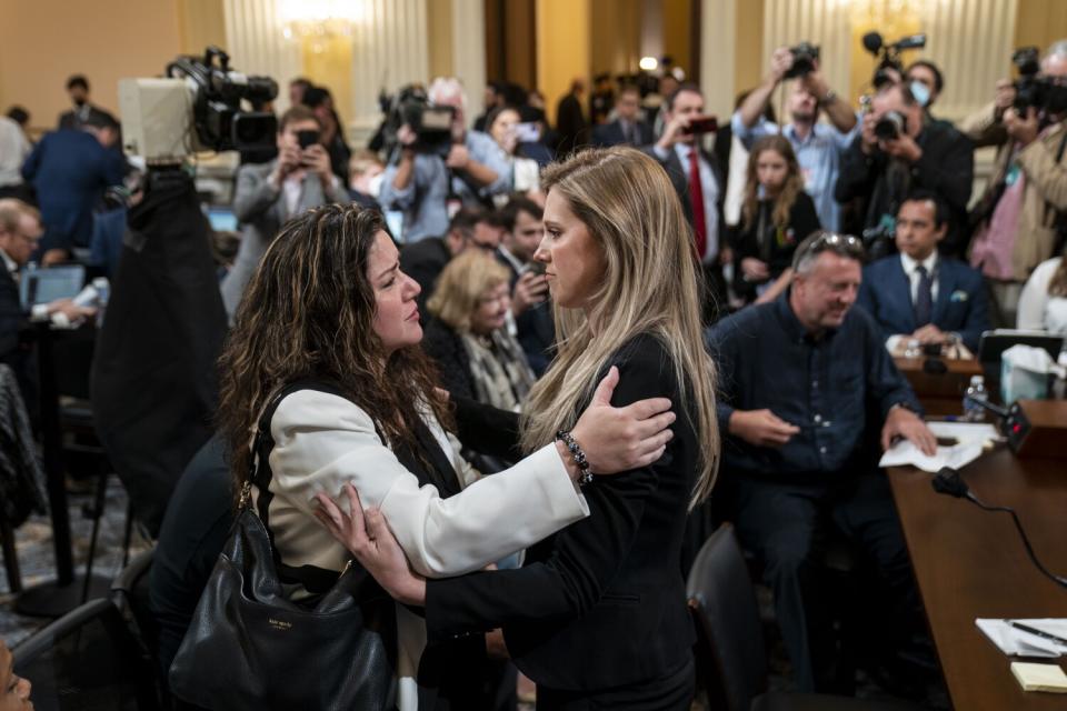 Two women half-embracing while speaking in a crowded room as photographers take pictures