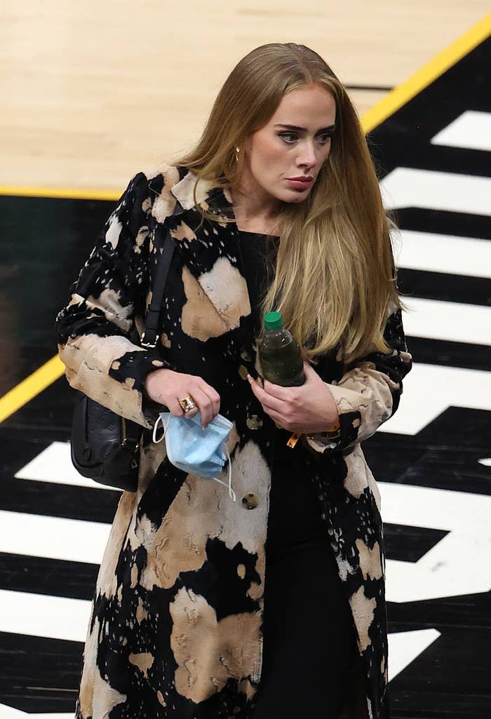 Adele holds a botled beverage and mask courtside at a basketball game