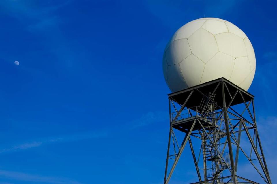 A Doppler radar tower is seen with the moon in the sky.
