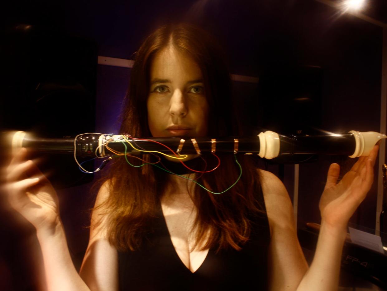 Liza Bec is in a dark room, holding up a recorder with peculiar wiring all around it.