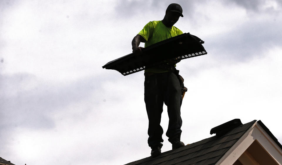 In this June 19, 2019, photo Larry McGee balances along a roof edge as he carries roof over ridge vent that he and others will be laying down on a new house in a Brandon, Miss., neighborhood. On Wednesday, July 17, the Commerce Department reports on U.S. home construction in June. (AP Photo/Rogelio V. Solis)