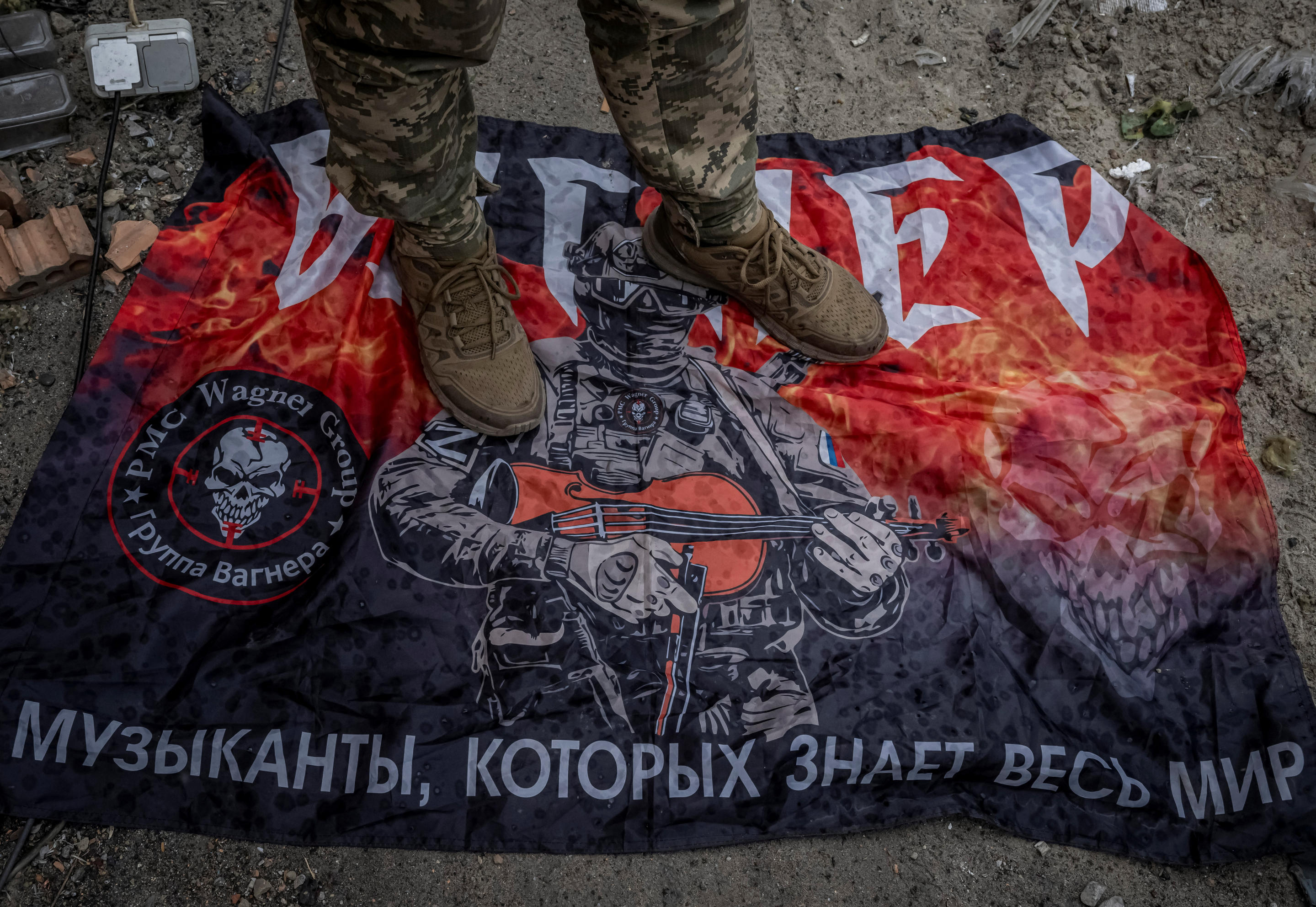 A Ukrainian serviceman stands on a flag of Russian mercenary group Wagner.