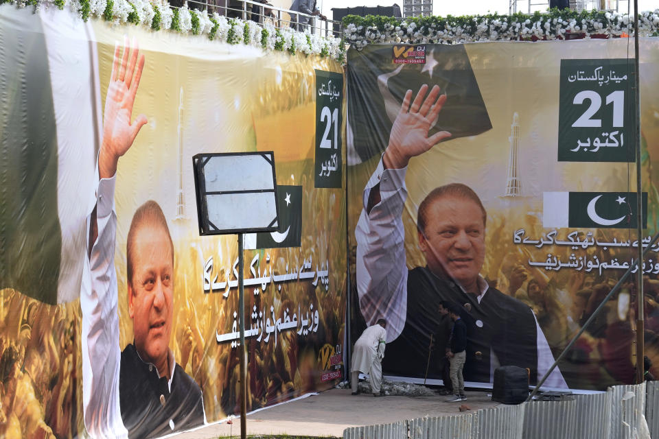 Workers give final touches next to huge portraits of Pakistan's former Prime Minister Nawaz Sharif displayed at the venue of his welcoming rally, in Lahore, Pakistan, Saturday, Oct. 21, 2023. Sharif was returning home Saturday on a special flight from Dubai, ending four years of self-imposed exile in London as he seeks to win the support of voters ahead of parliamentary elections due in January. (AP Photo/K.M. Chaudary)