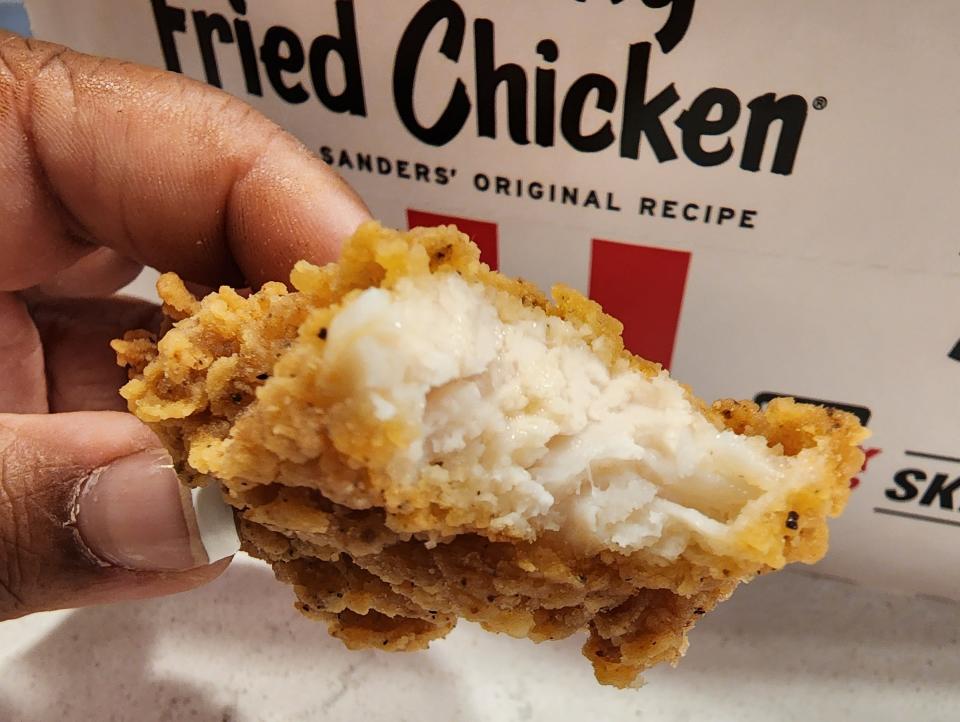 The writer holds a chicken tender with a bite taken out of it from KFC