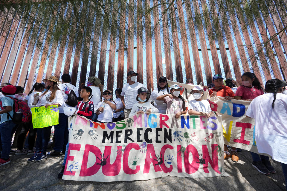 Young demonstrators hold a sign, that translates to 'migrant children deserve education,' standing along the border wall in Nogales, Sonora on Sept. 26, 2022. The sign is part of a march for migrants seeking asylum to protest Title 42, Border Patrol abuse against migrants, and lack of access to healthcare in Nogales.