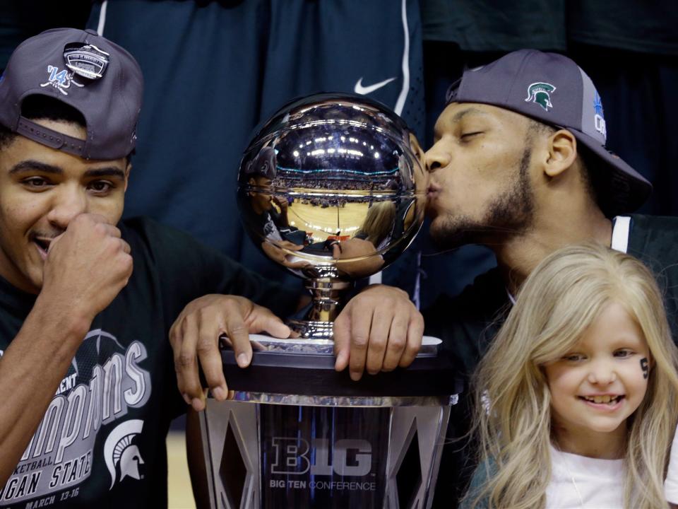 Adreian Payne kisses the Big Ten championship trophy while celebrating alongside teammate Gary Harris and friend Lacey Holsworth.