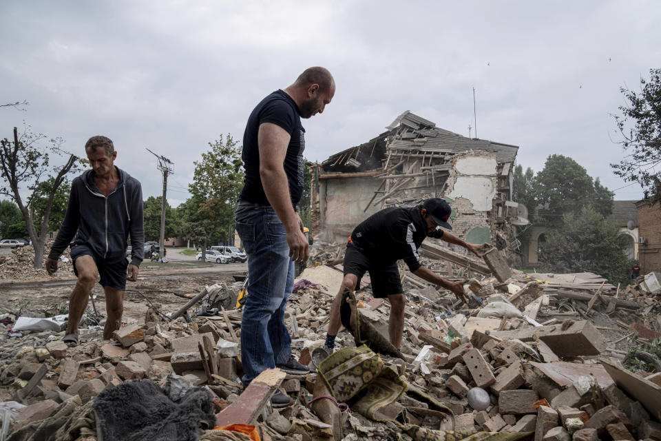 Local residents search for documents of their injured friend in the debris of a destroyed apartment house after Russian shelling in a residential area in Chuhuiv, Kharkiv region, Ukraine, Saturday, July 16, 2022. (AP Photo/Evgeniy Maloletka)