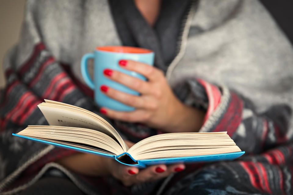 woman reading a book and holding a mug of hot beverage recovering from long covid