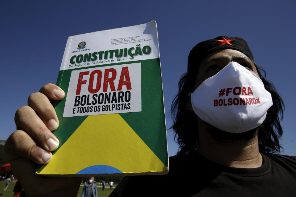 A demonstrator holds a copy of the Brazilian Constitution, during a protest demanding President Jair Bolsonaro be impeached, in front of the National Congress in Brasilia, Brazil, Thursday, May 21, 2020. As Brazil careens toward a full-blown public health emergency and economic meltdown, opponents have filed a request for Bolsonaro's impeachment based on his mishandling of the new coronavirus pandemic. (AP Photo/Eraldo Peres)