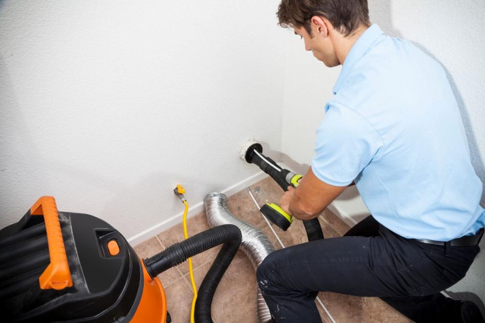 A man in a blue shirt installs a dryer vent.