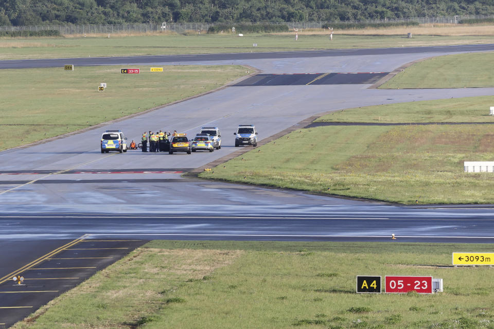 Security personnel and police officers stand near climate activists from the group Last Generation who have stuck themselves on a tarmac at Hamburg Airport, Germany, Thursday July 13, 2023. (Bodo Marks/dpa via AP)