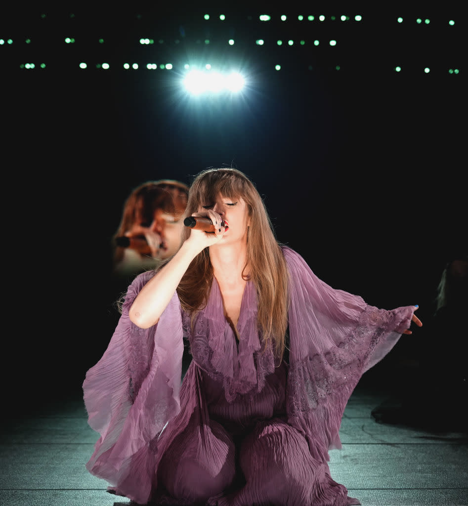 Person performing on stage in a flowing purple outfit with stage lights in the background