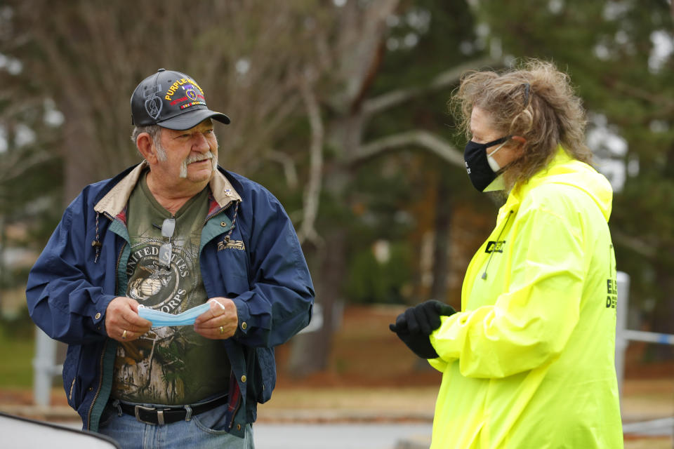 An Election Defender volunteer, right, talks to a voter after handing him a mask during early voting for the Senate runoff election, at Ron Anderson Recreation Center, Thursday, Dec. 17, 2020, in Powder Springs, Ga. (AP Photo/Todd Kirkland)