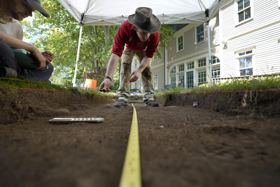 FILE — University of Massachusetts Boston graduate students Sean Fairweather, of Watertown, Mass., left, and Alex Patterson, of Quincy, Mass., right, use measuring instruments while mapping an excavation site, Wednesday, June 9, 2021, on Cole's Hill, in Plymouth, Mass. The archaeologists are part of a team excavating the grassy hilltop that overlooks iconic Plymouth Rock one last time before a historical park is built on the site. David Landon, not shown, of the University of Massachusetts-Boston's Fiske Center for Archaeological Research, says his team unearthed a cache of personal items he thinks were buried there in the late 1800s, most likely by a brokenhearted settler who had outlived all three of her children. (AP Photo/Steven Senne, File)