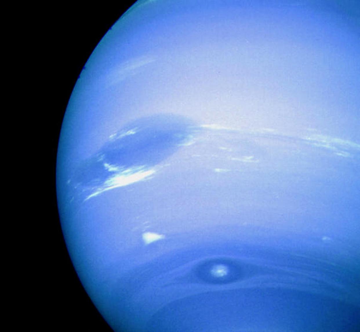 This NASA Voyager 2 image released 21 August, 2001 shows that the planet Neptune has spots. The Solar System's outermost gas giant shows a nearly uniform blue hue created by small amounts of methane drifting in a thick atmosphere of nearly colorless hydrogen and helium. Dark spots do appear, however, that are anti-cyclones: large high-pressure systems that swirl in Neptune's cold cloud tops. Two dark spots are visible in the above picture taken by the Voyager 2 spacecraft in 1989: an Earth-sized Great Dark Spot located on the far left, and Dark Spot 2 located near bottom. A bright cloud dubbed Scooter accompanies the Great Dark Spot. Subsequent images of Neptune by the Hubble Space Telescope in 1994 indicated that both of these dark spots had dissipated, but another had been created.  AFP PHOTO (Photo by NASA / NASA / AFP) (Photo by NASA/NASA/AFP via Getty Images)