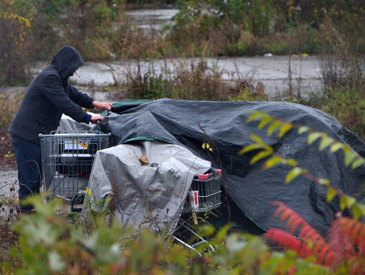 In a file photo, a man pulls a tarp over a tent in a homeless encampment behind Walgreens on Park Avenue.