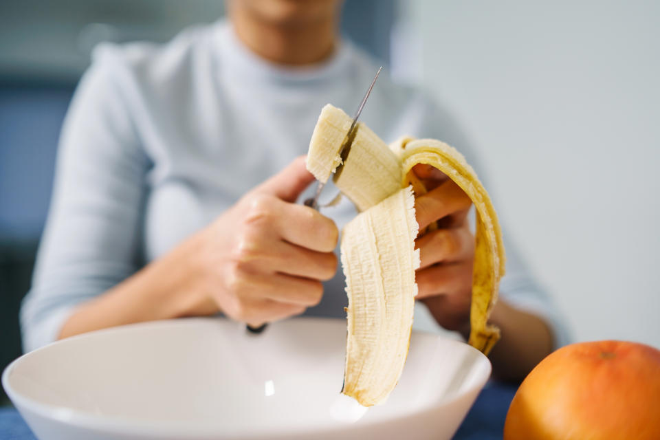 Caucasian woman sitting by the table at home cutting banana