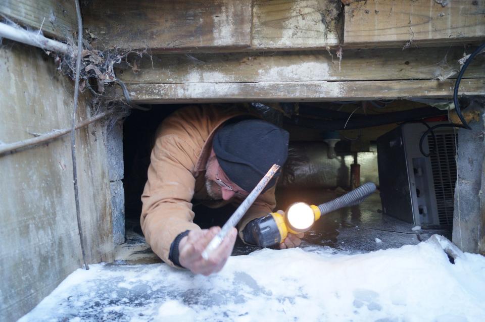 Paul McConnell, who slid into a crawlspace partially flooded with frozen water, holds up a shard of ice as he exits the cellar at a Georgetown home on Thursday, Feb. 19, 2015. The home’s water pipes froze, then burst, during a spell of record cold temperatures.
