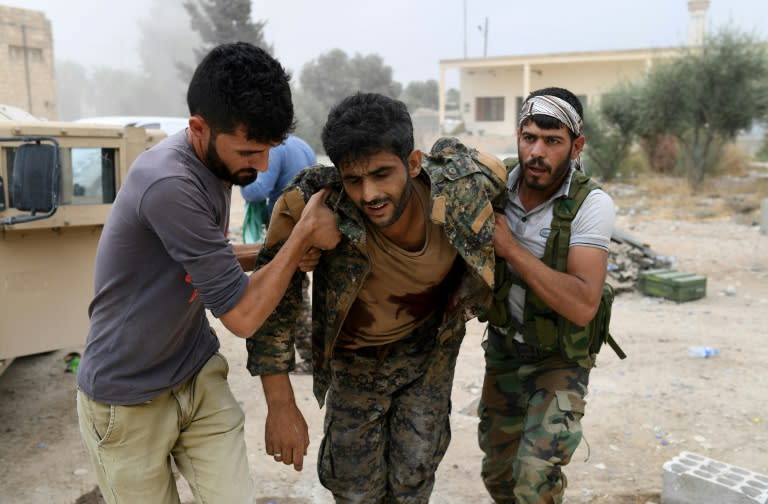 Members of the Syrian Democratic Forces carry wounded comrade Ibrahim (C) towards an armoured vehicle to drive him to a medical centre after he was shot by a jihadist sniper on the eastern frontline of Raqa