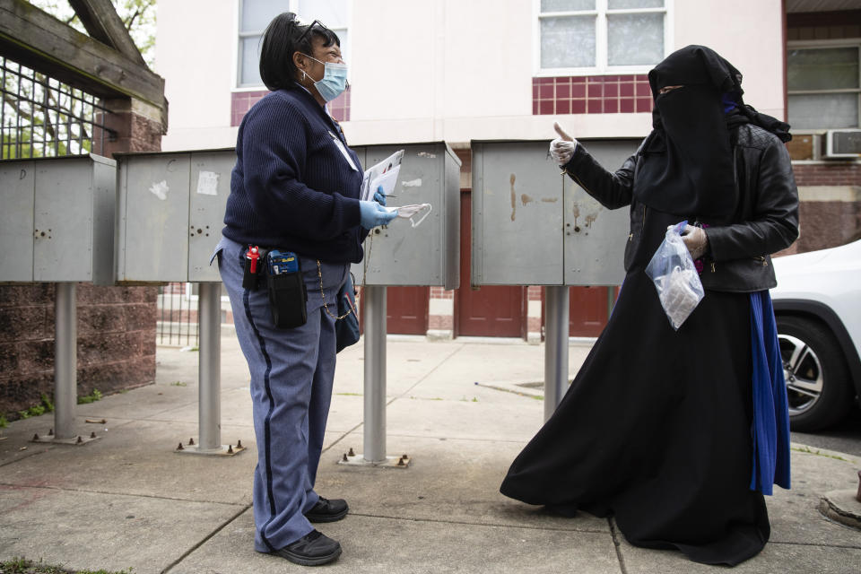 In this Wednesday, May 6, 2020, photo, Sharae Cunningham, right, gestures after giving United States Postal Service carrier Henrietta Dixon a protective face mask as she walks her rout to deliver mail in Philadelphia. (AP Photo/Matt Rourke)