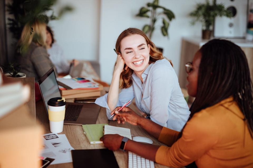 two coworkers smiling while sitting at a desk doing work