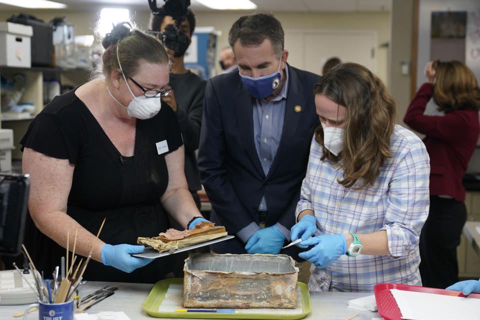 Virignia Gov. Ralph Northam, center, watches as lead conservator for the Virginia Department of Historic Resources, Kate Ridgway, left, and Sue Donovon, conservator for Special Collections for the University of Virginia, right, remove the contents of a time capsule that was removed from the pedestal that once held the statue of Confederate General Robert E. Lee on Monument Ave. Wednesday Dec. 22, 2021, in Richmond, Va. Three books and an envelope with a photo were inside the box. (AP Photo/Steve Helber)