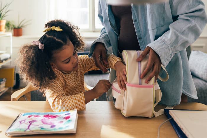 A child and an adult are packing a backpack at a table with a colorful drawing on it