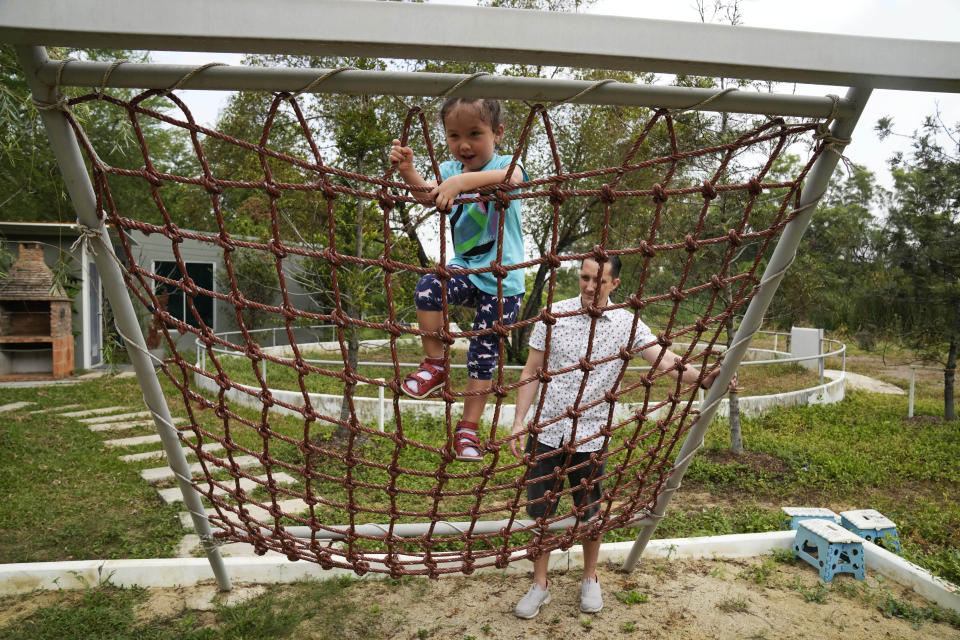 Richard Poulin, right, watches his daughter, Rylae-Ann Poulin, climb a rope ladder at a playground in Bangkok, Thailand, Saturday, Jan. 14, 2023. (AP Photo/Sakchai Lalit)