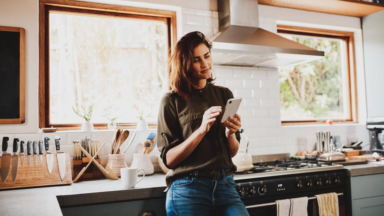 Cropped shot of an attractive young woman using a smartphone while standing in her kitchen at home.