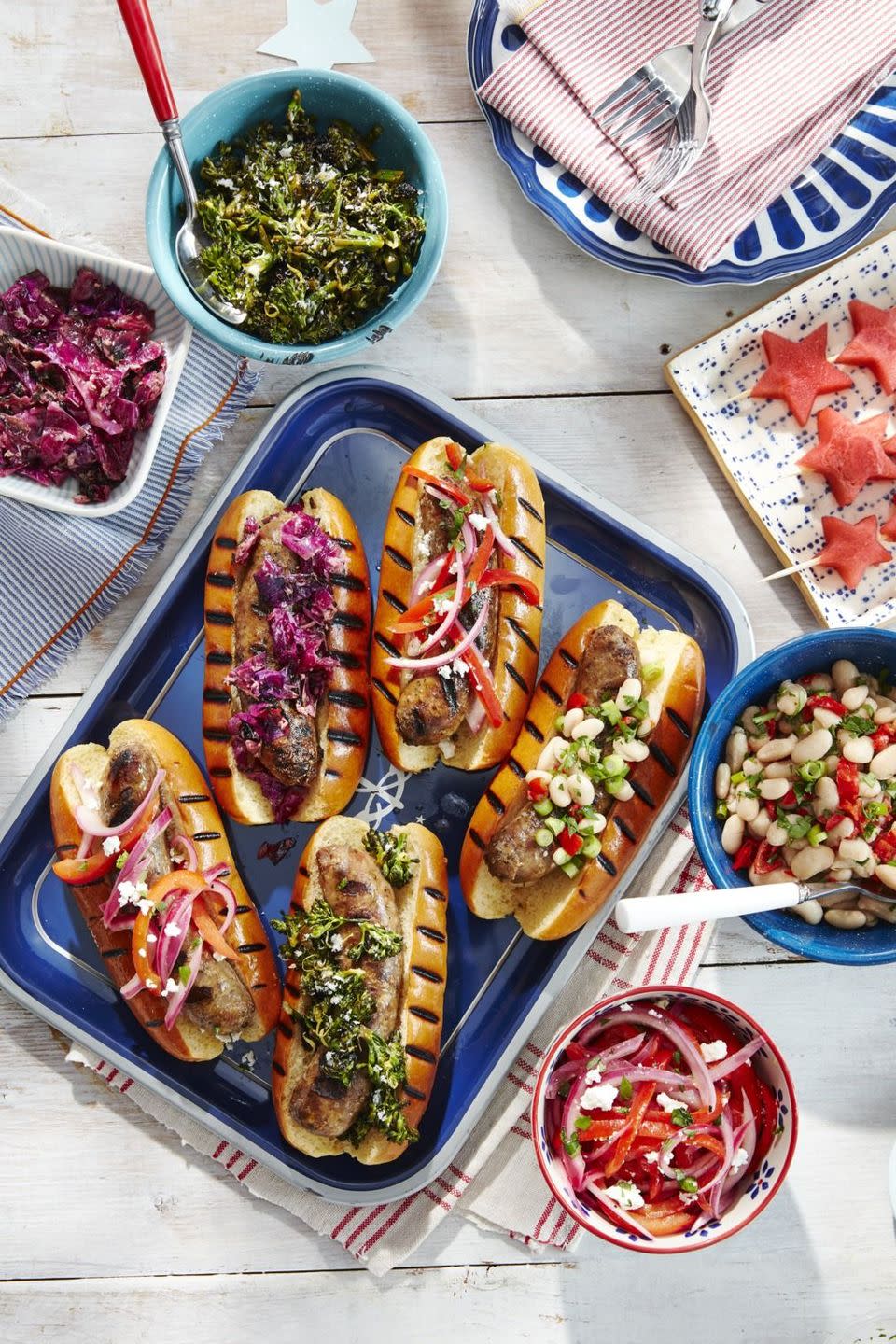 grilled sausages in grilled buns with various toppings on a dark blue serving tray