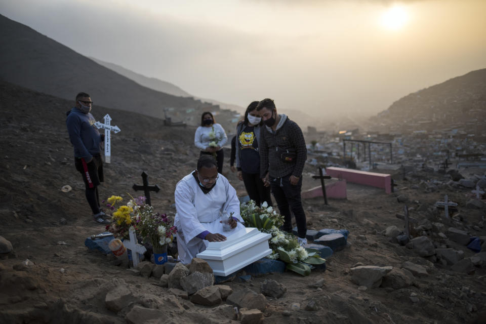 El hermano Ronald Marín, un laico venezolano de 30 años, reza sobre el ataúd que contiene los restos de la hija no nacida de Keizer Quiñones y Sarai Araujo en el cementerio "Mártires 19 de Julio" en Comas, en las afueras de Lima, Perú, el martes 21 de julio de 2020. Marín es uno de los pocos representantes de la Iglesia católica que administra funerales en el cementerio lejos del centro de la capital que parece una ciudad en miniatura encajada entre dos colinas desérticas. (AP Foto/Rodrigo Abd)